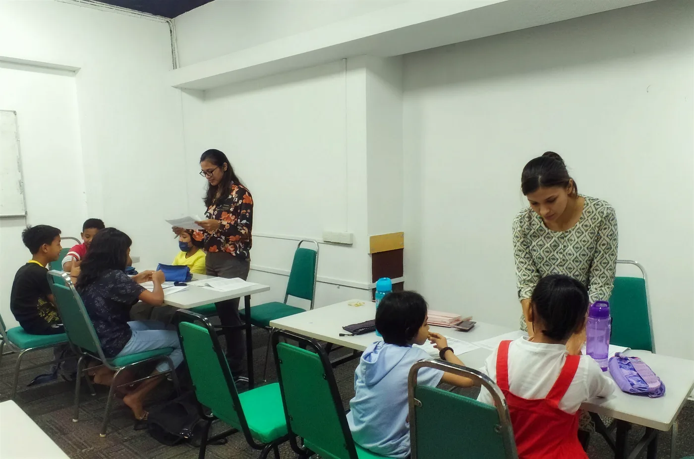 Dua guru membantu murid sekolah rendah di meja